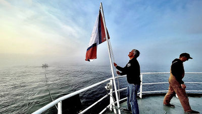 OceanGate Expeditions CEO Stockton Rush raises the mission flag on the stern of the Polar Prince in May. The Titan submersible, towed behind the ship, is in the background.